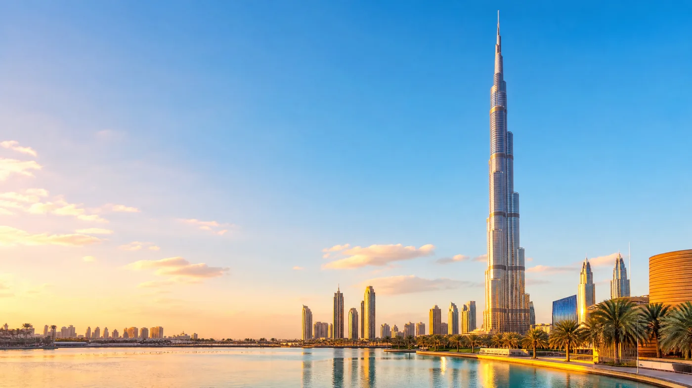 برج خليفة عبر بحيرة برج خليفة الهادئة في الساعة الذهبية، والنخيل والمباني المنخفضة عند قاعدته